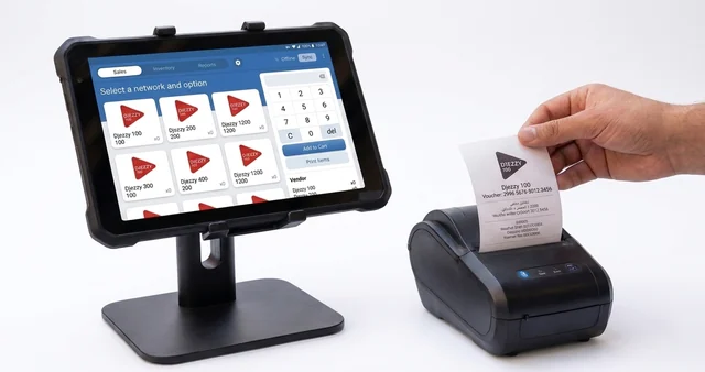 A rugged Android tablet on a counter stand running the voucher point-of-sale app, beside a small receipt printer, as a hand pulls a freshly printed voucher slip.